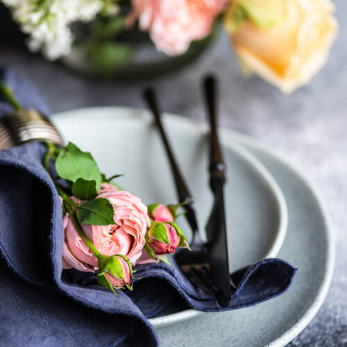 Festive table setting with beautiful roses, modern plates and cutlery on rustic grey background with copy space